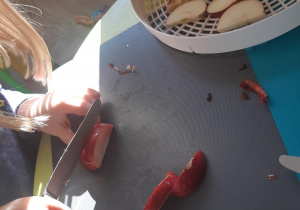 Dziewczynka stoi przy stoliku i kroi nożem jabłko.