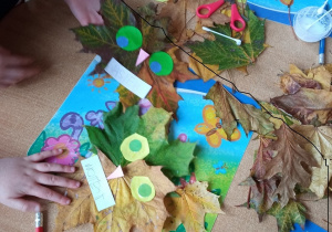 Dzieci prezentują sowy wykonane z liści i kolorowego papieru.