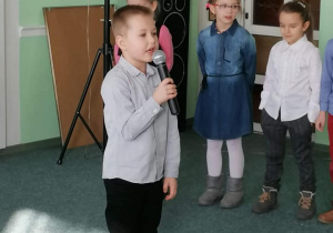 Chłopiec mówi do mikrofonu, w tle stoją trzy dziewczynki