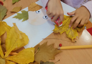 Dziewczynka przykleja liść tworząc włosy Pani Jesieni.