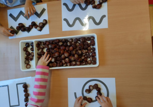 Dzieci układają wzory z kasztanów.