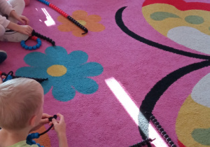 Dzieci siedzą na dywanie. Rozwiązują zadania na dodawanie na koralach matematycznych.