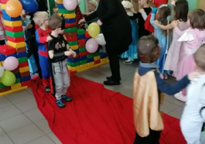 Nauczycielka przeprowadza dzieci przez magiczną bramę do krainy bajkowego karnawału.