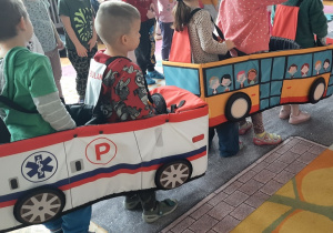 Dzieci poruszają się po macie - jezdni - w "autochodzikach": ambulansie i autobusie.