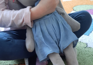 Dziewczynka siedzi na dywanie. W rączkach trzyma swoją przytulankę - króliczka.
