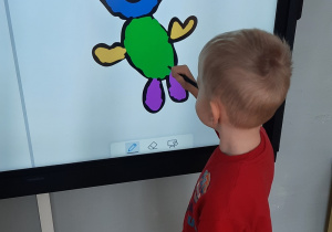 Chłopiec na monitorze multimedialnym rysuje misia.
