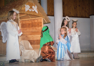 Przed szopką klęczą dzieci jako Józef i Maryja. Obok stoją trzy dziewczynki – anioły.