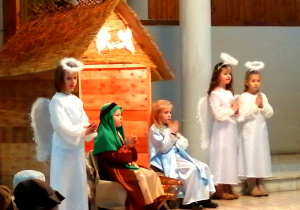 Józef i Maryja siedzą przy żłobku. Obok stoją trzy anioły.