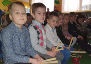 Dzieci siedzą na ławce, w dłoniach trzymają instrumenty muzyczne