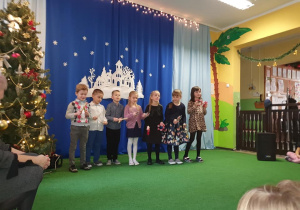 Dzieci stoją na scenie, w tle świąteczna dekoracja.
