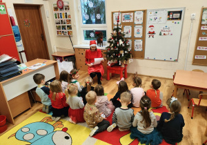 Nauczycielka siedzi na krześle i czyta opowiadanie od Mikołaja.