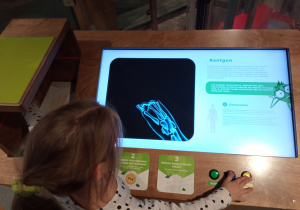 Dziewczynka prześwietla swoją rękę urządzeniem, które pokazuje na jakiej zasadzie działa rentgen.