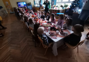Dzieci siedzą przy stole i jedzą czerwony barszcz.