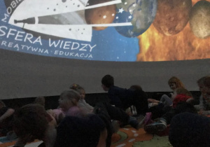 Dzieci są w środku kopuły planetarium, oglądają zdjęcia kosmosu.