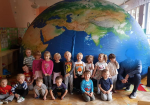 Dzieci pozują do zdjęcia przed mobilnym planetarium, które wygląda jak nasza planeta Ziemia.