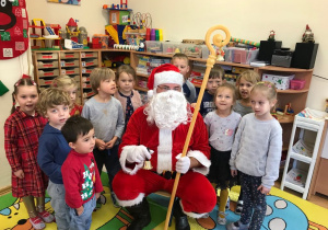 Dzieci z grupy czerwonej pozują do zdjęcia z Mikołajem. Uśmiechają się, machają rączkami.