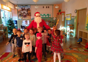 Dzieci z grupy zielonej pozują do zdjęcia z Mikołajem na scenie. Machają rączkami, pokazują czekoladowe Mikołaje.