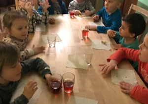 Dzieci siedzą przy dużym stole, jedzą ciasteczka i piją soczek.