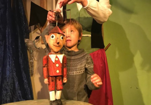 Na scenie stoi chłopiec i aktorka. Chłopiec posługuje się marionetką Pinokia.
