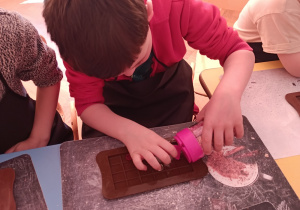 Chłopiec dekoruje formę na czekoladę - używa słodkiej posypki.