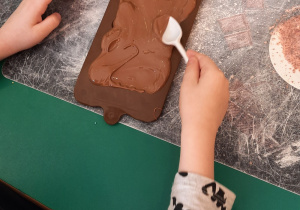 Chłopiec za pomocą plastikowej łyżeczki rozsmarowuje czekoladę w formie.