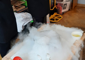 Eksperyment z wykorzystaniem suchego lodu - z naczynia stojącego na stoliku wydobywa się piana i mgła.