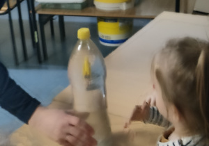 Dziewczynka bierze udział w eksperymencie - za pomocą ręki wprawia w ruch ludzika umieszczonego w butelce.