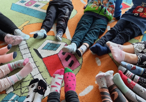 Dzieci siedzą na dywanie i prezentują kolorowe skarpetki.