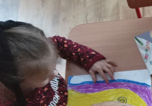 Dziewczynka rysuje twarz kobiety pastelami olejnymi.