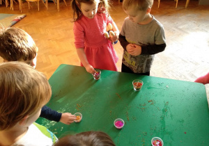 Dzieci stoją na początku stołu, oglądają stojące na nim, gotowe świece.
