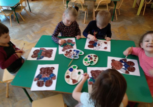Dzieci malują postać misia farbami.