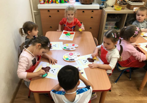 Dzieci siedzą przy stoliku, malują misia farbami przy pomocy gąbek.