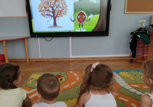 Dzieci oglądają film przyrodniczy na temat jesieni.
