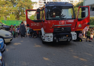 Wóz strażacki na terenie przedszkola, który oglądają dzieci.