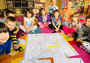 Dzieci siedzą na dywanie układają puzzle godło Polski.