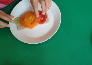 Dziewczynka układa pomidora na kanapce.