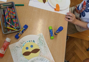Dzieci przy stoliku tworzą portret kucharza z wykorzystaniem papierowych talerzyków.