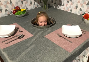 Magiczny stół. Dziewczynka siedzi pod stołem, na środku stołu widać jej głowę.