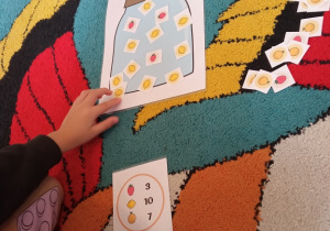 Dziecko układa obrazki owoców na papierowym słoiku według instrukcji.