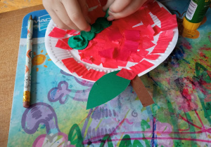 Chłopiec przykleja do papierowego talerzyka plastelinę, tworząc gąsienicę.