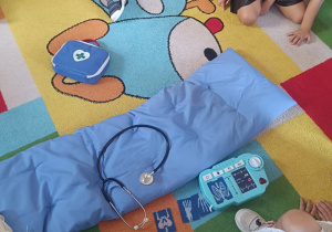 Dzieci na dywanie oglądają atrybuty lekarskie.