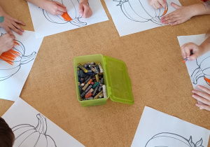 Dzieci przy stoliku kolorują pastelami dynie.