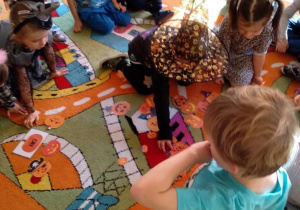 Dzieci siedzą na dywanie, segregują małe i duże obrazki dyni.