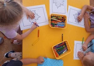 Dzieci kolorują kredkami obrazek jesiennego liścia.