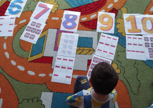 Chłopiec układa na dywanie kartę z symbolem narodowym przy odpowiedniej cyfrze.