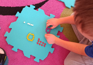 Chłopiec z darów zabawy Froebla układa na piankowym puzzlu literki.