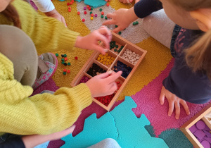 Dzieci sprzątają po zabawie - segregują dary zabawy Froebla według koloru.