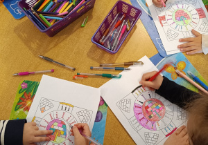 Dzieci przy stoliku kolorują literkowe mandale.