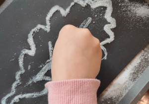 Dziewczynka sypie sól na szablon liścia pomalowany wcześniej białym klejem.