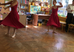 Baletnice ubrane w czerwone suknie wykonują obroty.